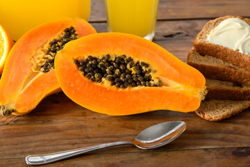 Papaya halves on wooden table with bread and juice