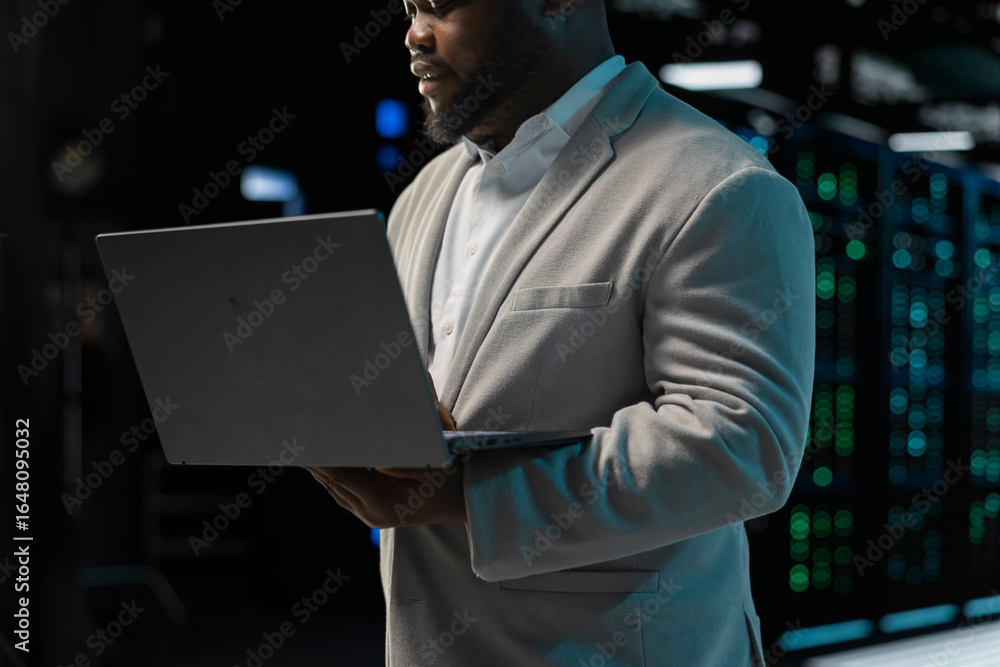 Poster close up of admin in server farm managing infrastructure systems, checking recovery plan on laptop. 