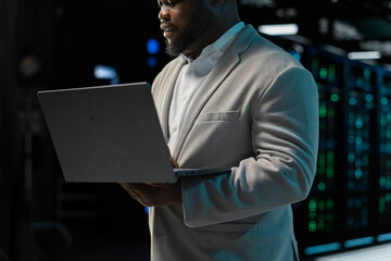 Close up of admin in server farm managing infrastructure systems, checking recovery plan on laptop....