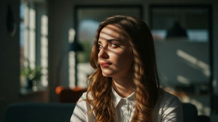 Young woman with long wavy brown hair illuminated by sunlight streaming through window blinds, casting striped shadows on her face - Powered by Adobe