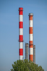 Two tall industrial smokestacks with red and white stripes against a clear blue sky