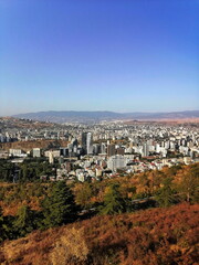 Elevated view of Tbilisi city in autumn, with colorful trees in the foreground and urban skyline...