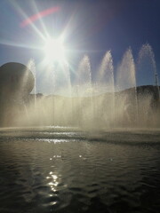 Backlit view of fountain jets in bright sunlight, creating sparkling spray and shimmering...