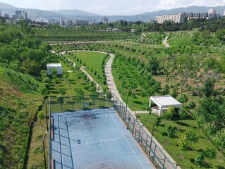 Aerial view of a fenced basketball court surrounded by walking paths, lawns, and landscaped...