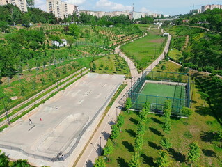Aerial view of a modern urban park with a skatepark, fenced football field, walking paths, and...