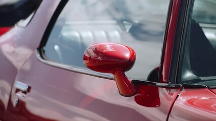 Jewel like rearview mirror on red classic sports coupe. Close up shot highlighting liquid curves - automotive haute couture in daylight. 