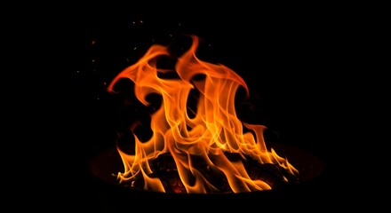 Orange flames dancing on burning wood logs with glowing embers and sparks against black background for fireplace concepts