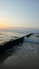 sunset on the beach Wooden breakwater stretching into the sea at sunset, with gentle waves and warm...