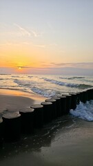 sunset on the beach Wooden breakwater stretching into the sea at sunset, with gentle waves and warm...