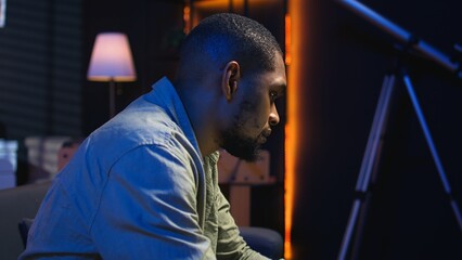 African American young adult working remotely on a laptop under loft neon lights, sitting on a...