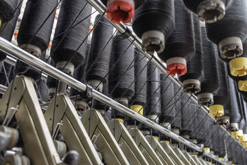 Black yarn cones on spinning machine in textile factory close up