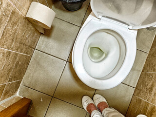 Toilet in a small restroom with toilet paper and a trash can on the side