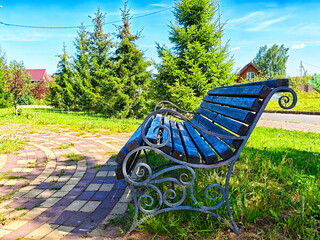Black metal bench in a green park setting surrounded by trees on a sunny day