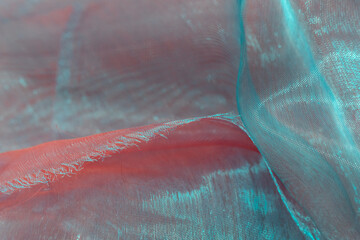Frayed sheer organza fabric in red and teal hues with iridescent shimmer, forming a romantic and...