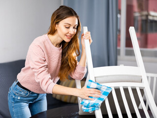 Young european woman cleaning up the apartment wipes a chair with a damp cloth