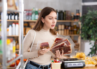 Young female shopper buying jamon meat in grocery store..