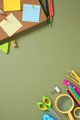Flat lay of colorful school supplies on green background with cork board. Creative workspace with...