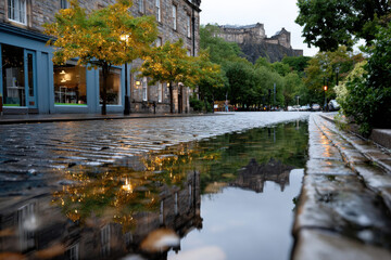 This photo showcases a cobblestone street in Edinburgh reflecting the castle above, creating a tranquil yet vibrant scene worthy of exploration and appreciation for its beauty.