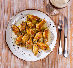 On plate is hearty snack - large portion of fried chicken wings with crispy crust, poured with thick barbecue sauce
