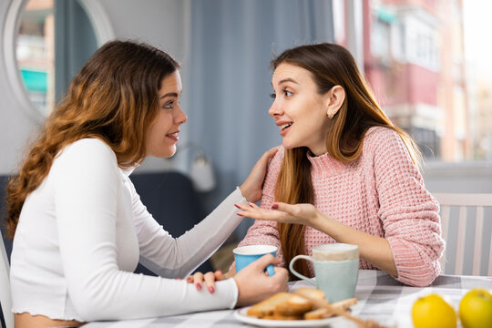 Two female friends have fun chatting while having tea at the table at home - Powered by Adobe