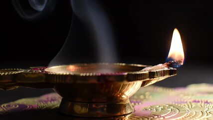 Traditional brass oil lamp (diya) with a flickering flame and rising smoke against a dark background, symbolizing light and spirituality. - Powered by Adobe