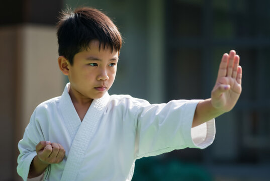Young Asian boy in a white gi practicing a karate block. Child with a focused expression during martial arts training.