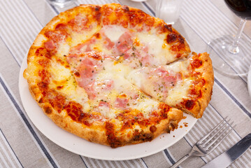 Oven-cooked Italian pizza with cheese and prosciutto close-up. Delicious sliced pizza with a stretchy cheese