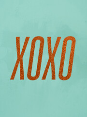XOXO word written in orange glitter font, hugs and kisses text message for social media or letter on teal or light turquoise green background with texture, shiny, flame-red, rust-colored confetti,