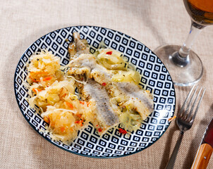 There are large pieces of Atlantic herring on plate. Fish is cooked with spicy salt curing with paprika, pepper and garnished by stewed cabbage.