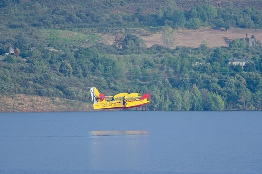 Firefighting seaplane flying over water, scooping water to extinguish wildfire in el bierzo, leon, spain