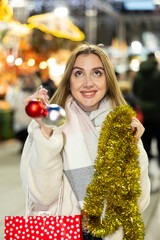 Merry Christmas - adorable girl with Christmas balls and tinsel walking through a street fair in...