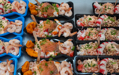 Sea street food for tourists on fish market on promenade in Oostende, Belgium, plastic box with variety of sea shells, shrimps, crab sticks, smoked fish