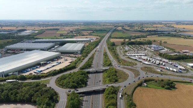 Aerial drone footage, busy motorway M1 and roundabout junction with industrial warehouses distribution centres and motorway services near Coventry England UK