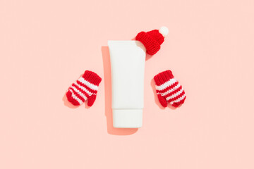 White plastic cosmetic tube with tiny hat and gloves on pink background