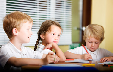 Primary students collaborating in a classroom. A candid view of three young children sitting together at a desk focused on their work or their teacher in class. From a series of images.