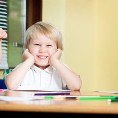 A happy primary school boy smiling. A cheerful young pupil sits at his classroom desk during a lesson, looking at the camera with a big, enthusiastic smile on his face. From a series of images.
