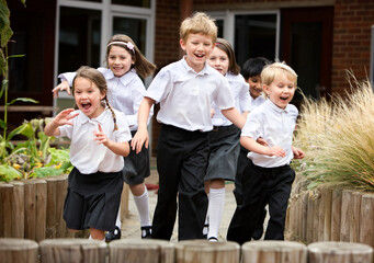 Cheerful primary students running outdoors. A group of happy children in school uniforms laughing and playing in a school playground during break time.