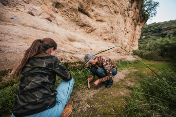 Mother and daughter hiking through the countryside, observing plants and rocks on a cliff, dressed...