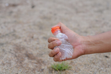 Close-up of a hand picking up a plastic drink bottle as waste. Concept of recycling, environmental protection, and waste management.