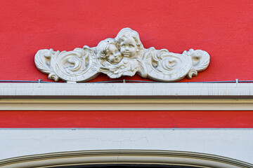 Detail of the red facade of an old house with a base-relief representing a pair of cherubs, putti, or angels, Italy