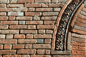 Close-up of an ancient brick wall with a decorative arch in terracotta, Italy