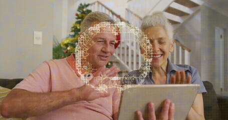 Waving at tablet, senior couple sitting on sofa at home, with Christmas tree and neural graphic
