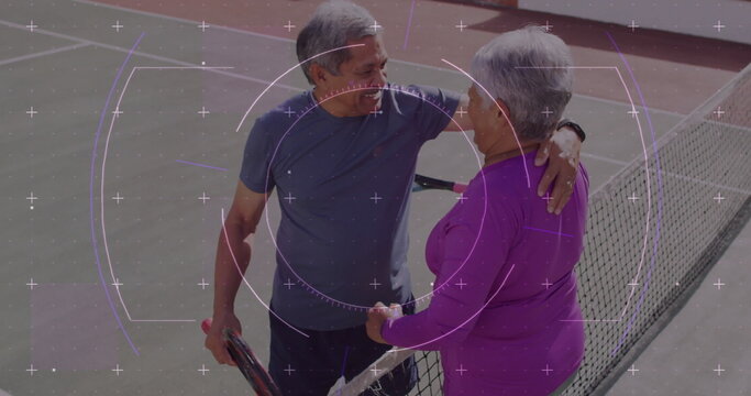 Hugging senior couple in sportswear on sunny tennis court with chain-link fence, rackets, net - Powered by Adobe