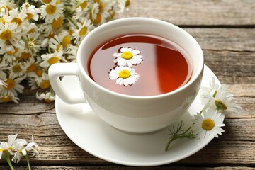 Aromatic tea in cup and chamomile flowers on wooden table, closeup