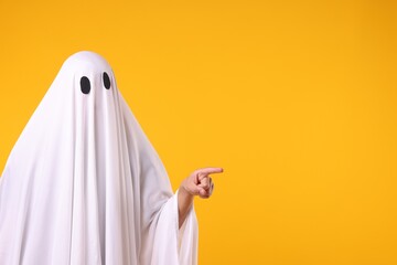 Man in ghost costume pointing at something on orange background. Space for text