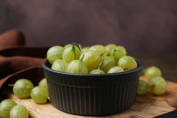 Fresh green gooseberries in bowl on table, closeup