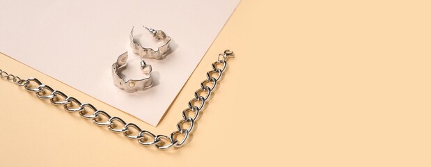 Beautiful silver bracelet and earrings on color background with space for text