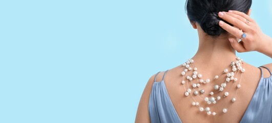 Young woman wearing beautiful pearl jewelry on light blue background with space for text, back view
