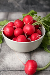 Bowl of ripe radish with green leaves on table