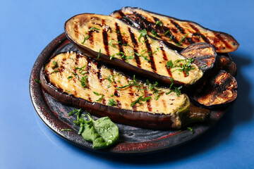 Plate with delicious grilled eggplants on blue background